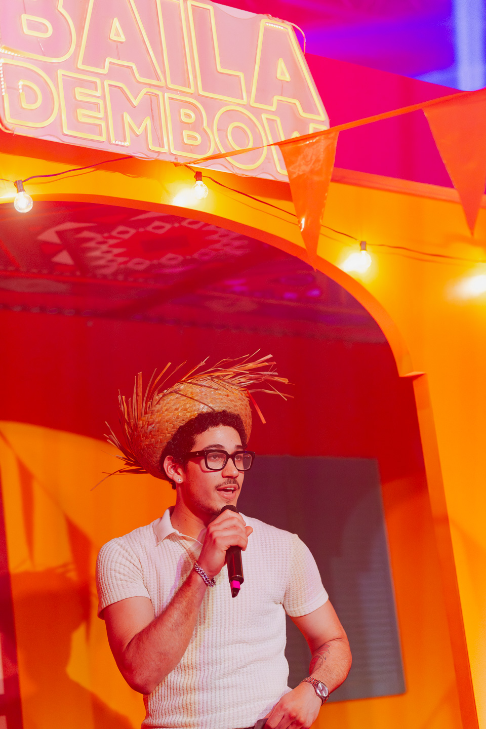 MC with mic under Baila Dembow sign